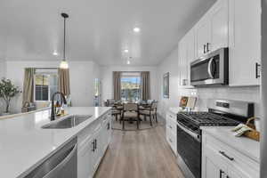 Kitchen with appliances with stainless steel finishes, white cabinets, hanging light fixtures, light wood-style floors, and healthy amount of natural light
