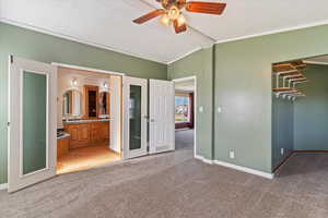 Unfurnished bedroom featuring light colored carpet, a textured ceiling, ensuite bathroom, lofted ceiling, and a walk in closet