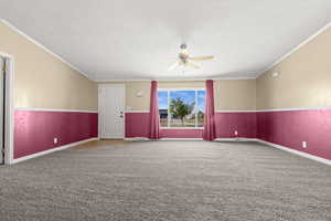 Unfurnished room with crown molding, a textured ceiling, carpet, a wainscoted wall, and ceiling fan