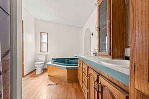 Bathroom featuring light wood finished floors, a textured ceiling, a garden tub, and double vanity
