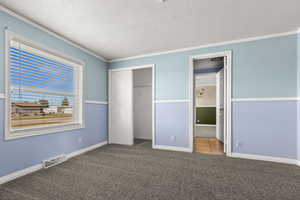 Unfurnished bedroom with a textured ceiling, carpet flooring, ornamental molding, and a closet