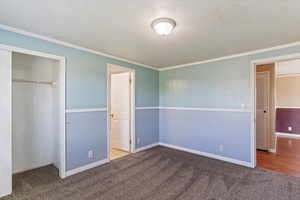 Unfurnished bedroom with carpet flooring, ornamental molding, a textured ceiling, and a closet
