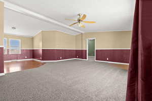 Carpeted spare room with a textured ceiling, a ceiling fan, crown molding, and a wainscoted wall