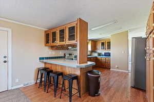 Kitchen featuring glass insert cabinets, a breakfast bar, brown cabinetry, ornamental molding, and light wood-style flooring