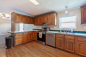 Kitchen featuring appliances with stainless steel finishes, a textured ceiling, brown cabinets, light wood-style flooring, and a peninsula