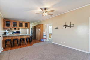 Kitchen with crown molding, glass insert cabinets, dark carpet, brown cabinetry, and a kitchen bar
