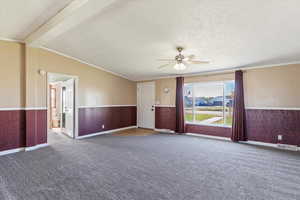 Carpeted spare room with a textured ceiling, a wainscoted wall, crown molding, beamed ceiling, and ceiling fan