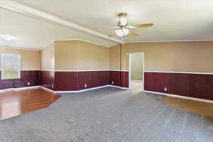 Spare room with a textured ceiling, carpet floors, a wainscoted wall, ornamental molding, and a ceiling fan