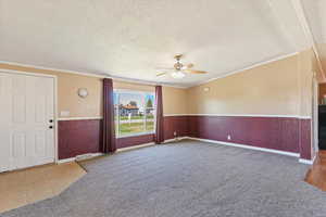 Unfurnished living room with wainscoting, ornamental molding, a textured ceiling, a ceiling fan, and light carpet