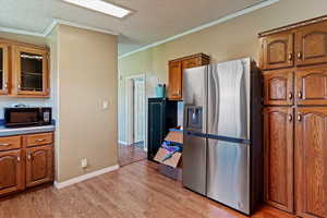 Kitchen with stainless steel fridge, brown cabinets, a textured ceiling, light wood finished floors, and crown molding