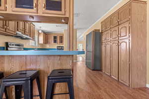 Kitchen featuring lofted ceiling, glass insert cabinets, light wood-style flooring, a kitchen breakfast bar, and stainless steel appliances