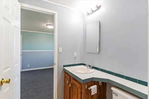 Bathroom with a textured ceiling, dark carpet, vanity, and crown molding