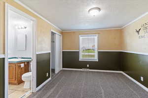Unfurnished bedroom with a textured ceiling, ornamental molding, carpet, a closet, and connected bathroom