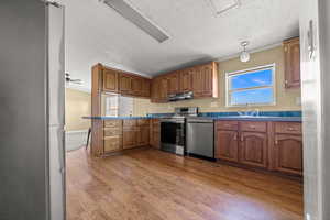 Kitchen featuring stainless steel appliances, brown cabinetry, light wood-type flooring, a textured ceiling, and a peninsula