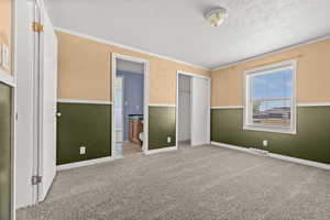 Unfurnished bedroom with a closet, crown molding, carpet floors, a textured ceiling, and ensuite bathroom