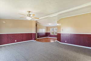 Spare room featuring a textured ceiling, wainscoting, carpet, ceiling fan, and crown molding