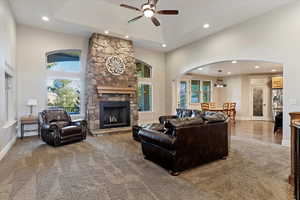 Carpeted living room featuring plenty of natural light, a stone fireplace, a high ceiling, a ceiling fan, and recessed lighting