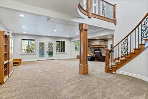 Unfurnished living room featuring french doors, a fireplace, light colored carpet, recessed lighting, and stairs