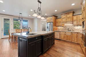 Kitchen with pendant lighting, light stone counters, backsplash, a kitchen island with sink, and appliances with stainless steel finishes