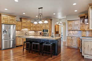 Kitchen featuring backsplash, arched walkways, stainless steel appliances, hanging light fixtures, and recessed lighting