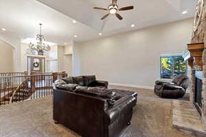 Carpeted living area with a stone fireplace, recessed lighting, a chandelier, a towering ceiling, and ceiling fan