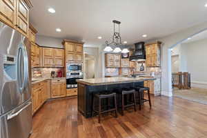 Kitchen featuring arched walkways, appliances with stainless steel finishes, backsplash, a kitchen breakfast bar, and decorative light fixtures