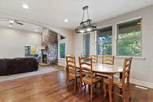 Dining room with wood-type flooring, a stone fireplace, recessed lighting, and arched walkways
