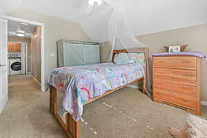 Bedroom with light carpet, washer / dryer, lofted ceiling, and ceiling fan