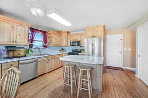 Kitchen featuring light brown cabinets, light countertops, appliances with stainless steel finishes, and light wood-style floors
