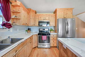Kitchen featuring appliances with stainless steel finishes, light brown cabinets, open shelves, light wood-style floors, and a textured ceiling