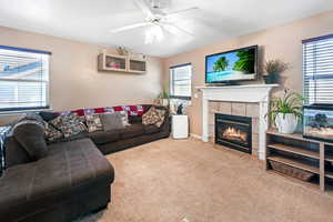 Living area with carpet flooring, a ceiling fan, and a tile fireplace