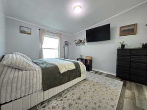 Bedroom with lofted ceiling, wood finished floors, a textured ceiling, and ornamental molding