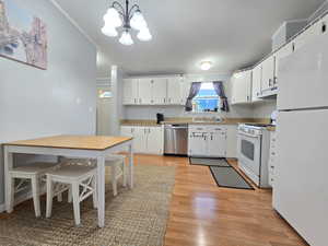 Kitchen with white appliances, white cabinetry, light wood-type flooring, a chandelier, and hanging light fixtures
