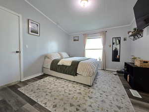 Bedroom with dark wood-type flooring, lofted ceiling, a textured ceiling, and ornamental molding