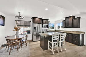 Kitchen featuring dark brown cabinetry, a center island, a kitchen bar, stainless steel appliances, and light wood-type flooring