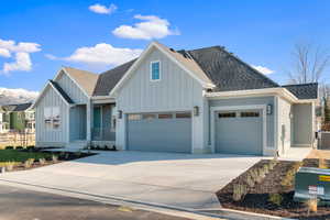 View of front facade with a shingled roof, board and batten siding, driveway, and a garage