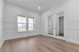 Spare room featuring a decorative wall, light wood-style floors, a wainscoted wall, and french doors