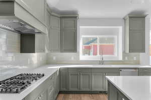 Kitchen featuring gray cabinets, premium range hood, backsplash, and appliances with stainless steel finishes