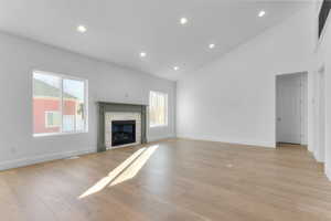 Unfurnished living room featuring high vaulted ceiling, light wood-style floors, a stone fireplace, healthy amount of natural light, and recessed lighting