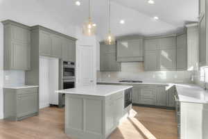 Kitchen with gray cabinetry, vaulted ceiling, a kitchen island, decorative light fixtures, and custom exhaust hood