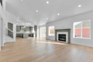 Unfurnished living room featuring recessed lighting, a fireplace, light wood-style floors, vaulted ceiling, and a chandelier