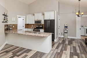 Kitchen with a peninsula, high vaulted ceiling, backsplash, stainless steel appliances, and light stone counters
