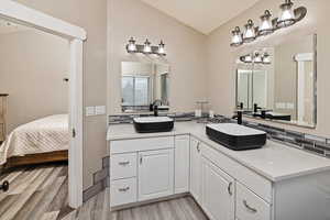 Full bath featuring double vanity, decorative backsplash, light wood-type flooring, vaulted ceiling, and ensuite bath