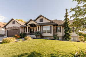 View of front of home with stucco siding, a front yard, a porch, stone siding, and an attached garage