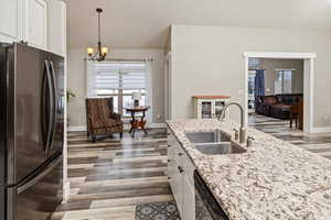Kitchen with white cabinets, freestanding refrigerator, light stone countertops, dark wood finished floors, and healthy amount of natural light