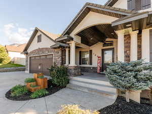 Property entrance with stone siding, covered porch, concrete driveway, stucco siding, and a ceiling fan