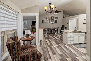Kitchen with vaulted ceiling, hanging light fixtures, white cabinets, light stone countertops, and light wood-style flooring