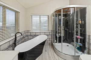 Full bath featuring a stall shower, lofted ceiling, a freestanding bath, tile walls, and light wood-type flooring
