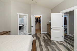 Bedroom featuring a walk in closet, dark wood-style floors, high vaulted ceiling, and ensuite bath