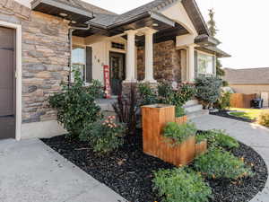 Property entrance with stone siding, covered porch, a garage, and stucco siding